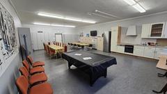 Blick in den Projektraum mit vielen Tischen und Stühlen und einer Küchenzeile und einen Billiardtisch
